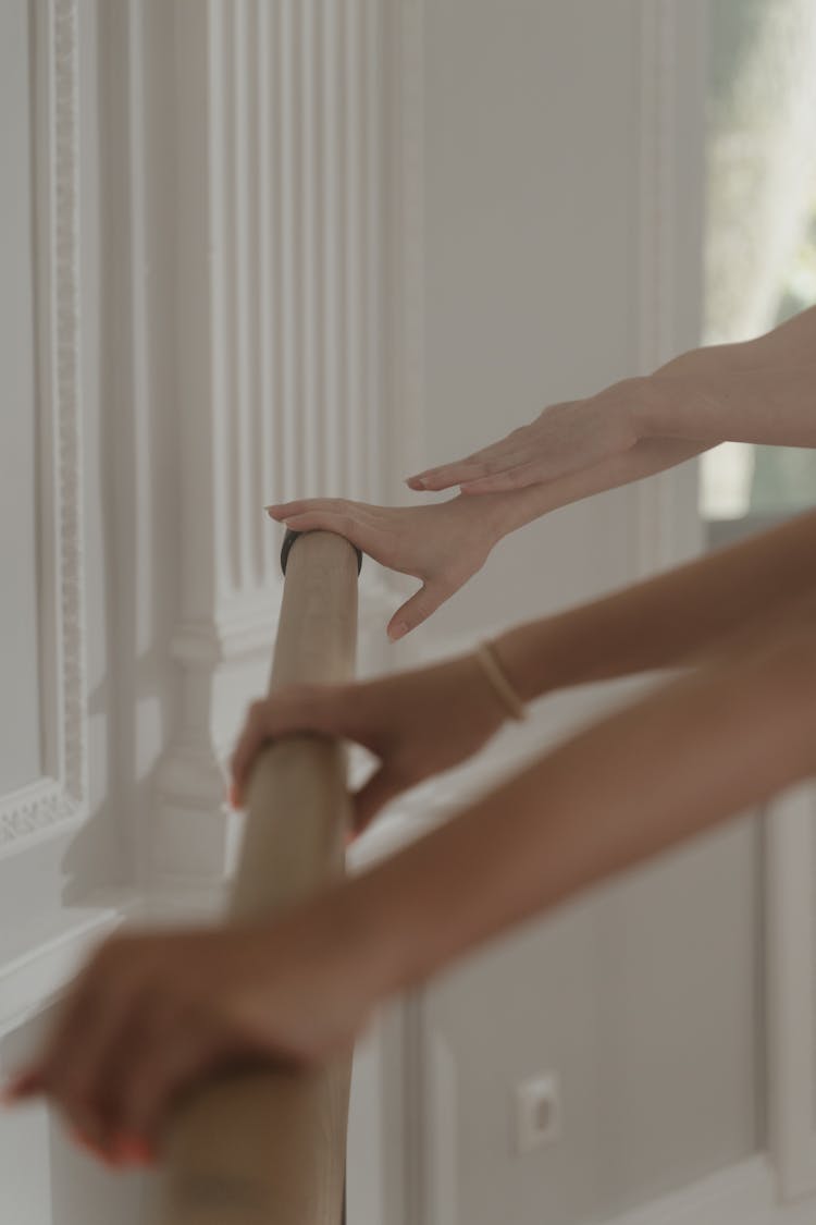 Hands Of People On Wooden Railing Near A White Wall