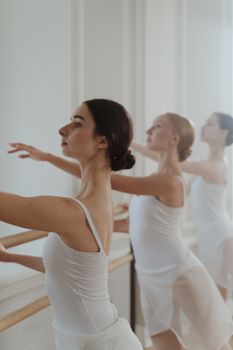 Three ballerinas practicing in a classical ballet class, captured in a vertical shot with soft lighting.