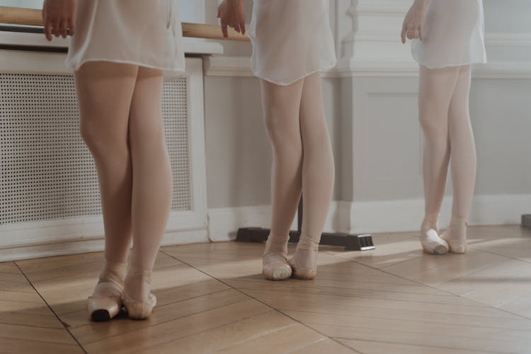 Three Ballerinas In White Skirts And Pointe Shoes Standing In Fifth Position