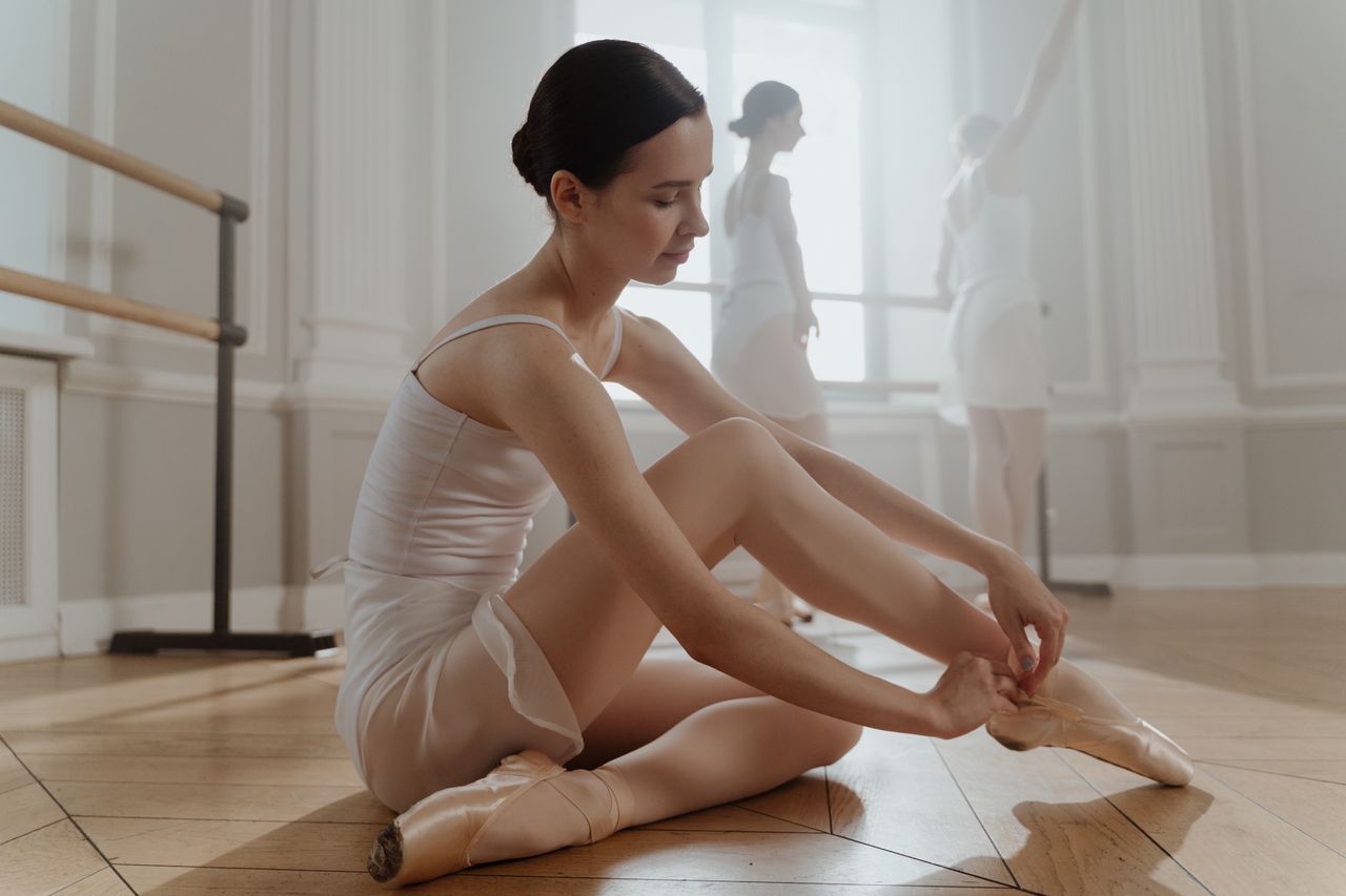 a graceful ballerina tying her shoes in a bright serene ballet studio