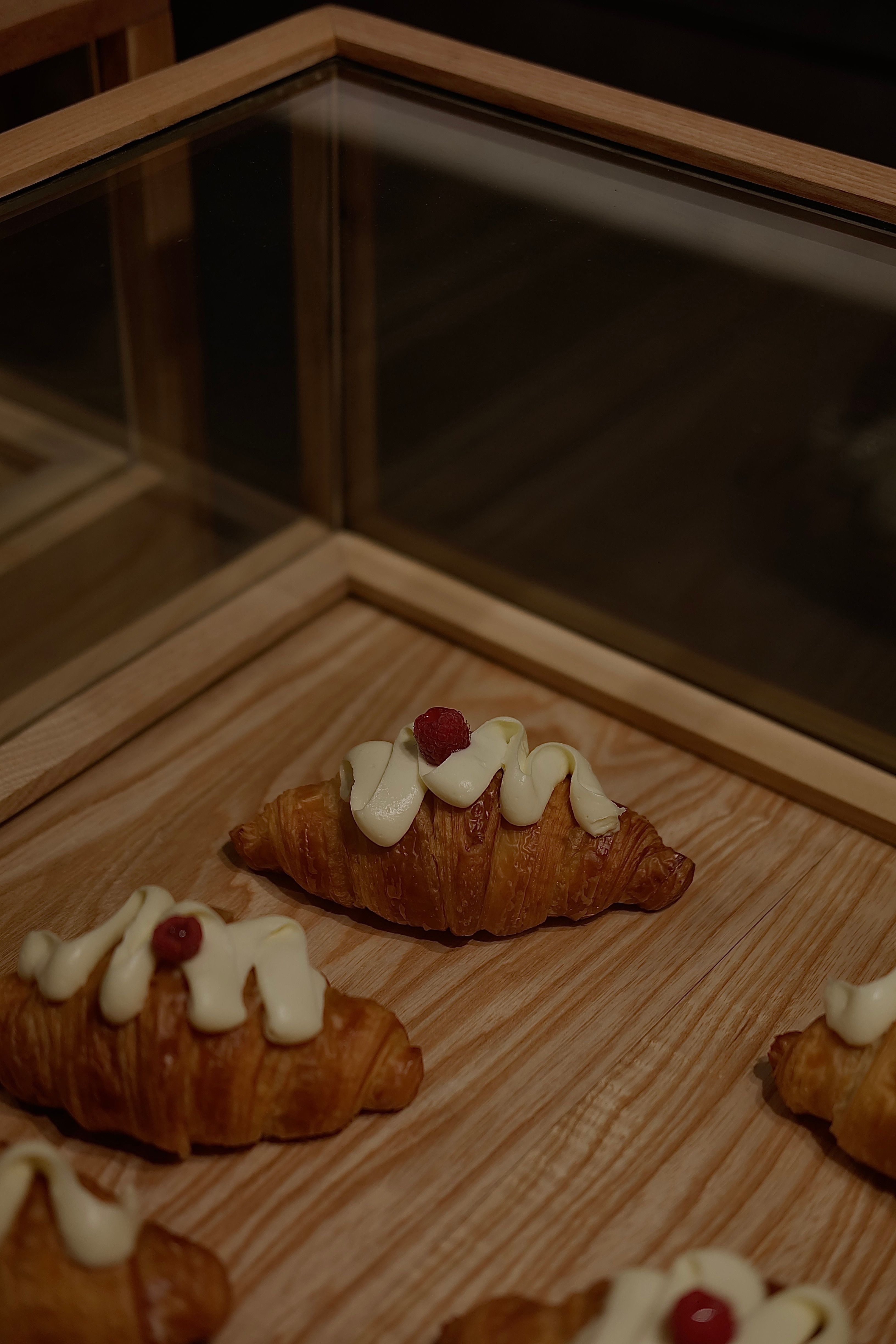 Delicious croissants topped with cream and berries displayed on a wooden tray.