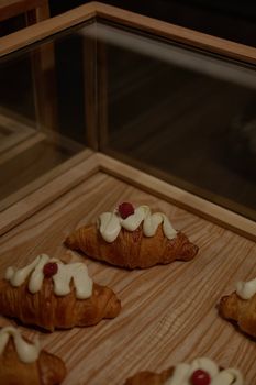 Delicious croissants topped with cream and berries displayed on a wooden tray.