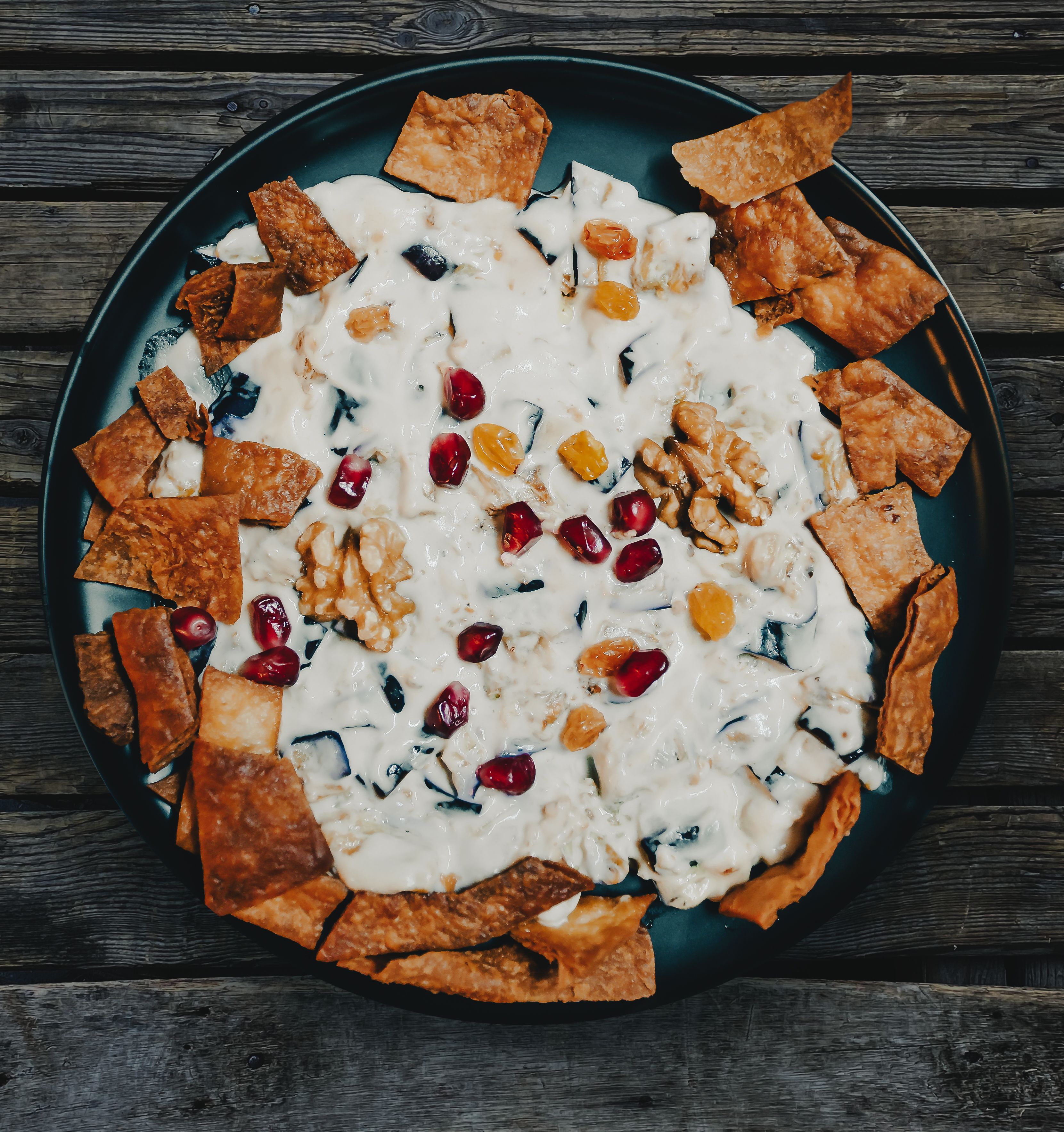Top view of a delicious creamy dessert with pomegranate and walnuts on a dark plate.