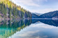 宁静的湖泊倒映着茂密的松林和远处的山峦，是理想的自然静谧背景