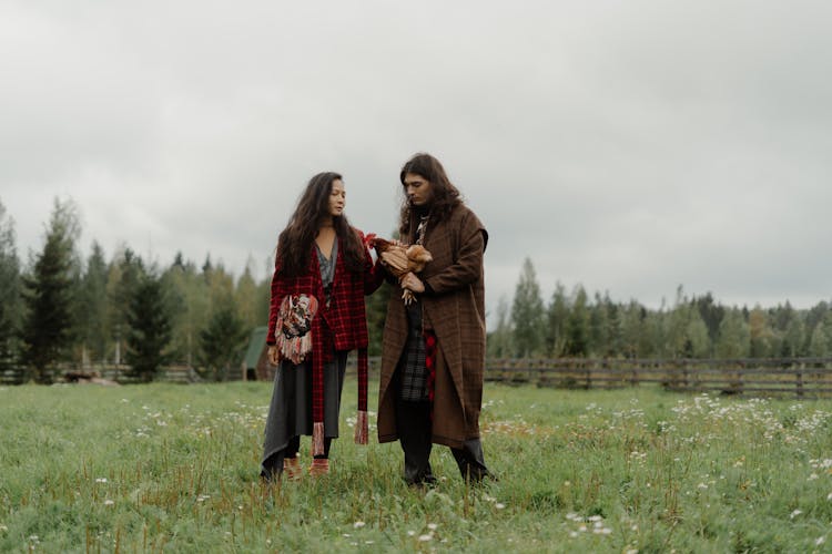 A Man And A Woman Holding A Chicken While Standing On Grass