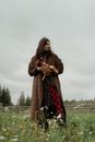 A Man in Brown Coat Standing on Green Grass while Carrying a Rooster