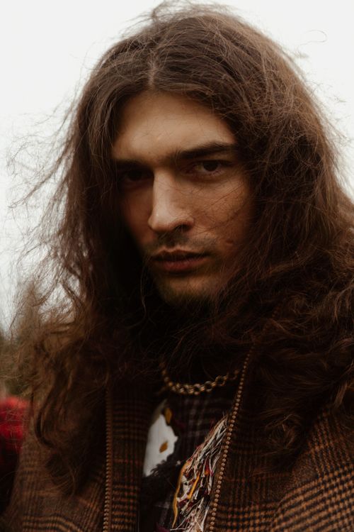 Free Close-up portrait of a long-haired man in a moody outdoor setting with a vintage style. Stock Photo