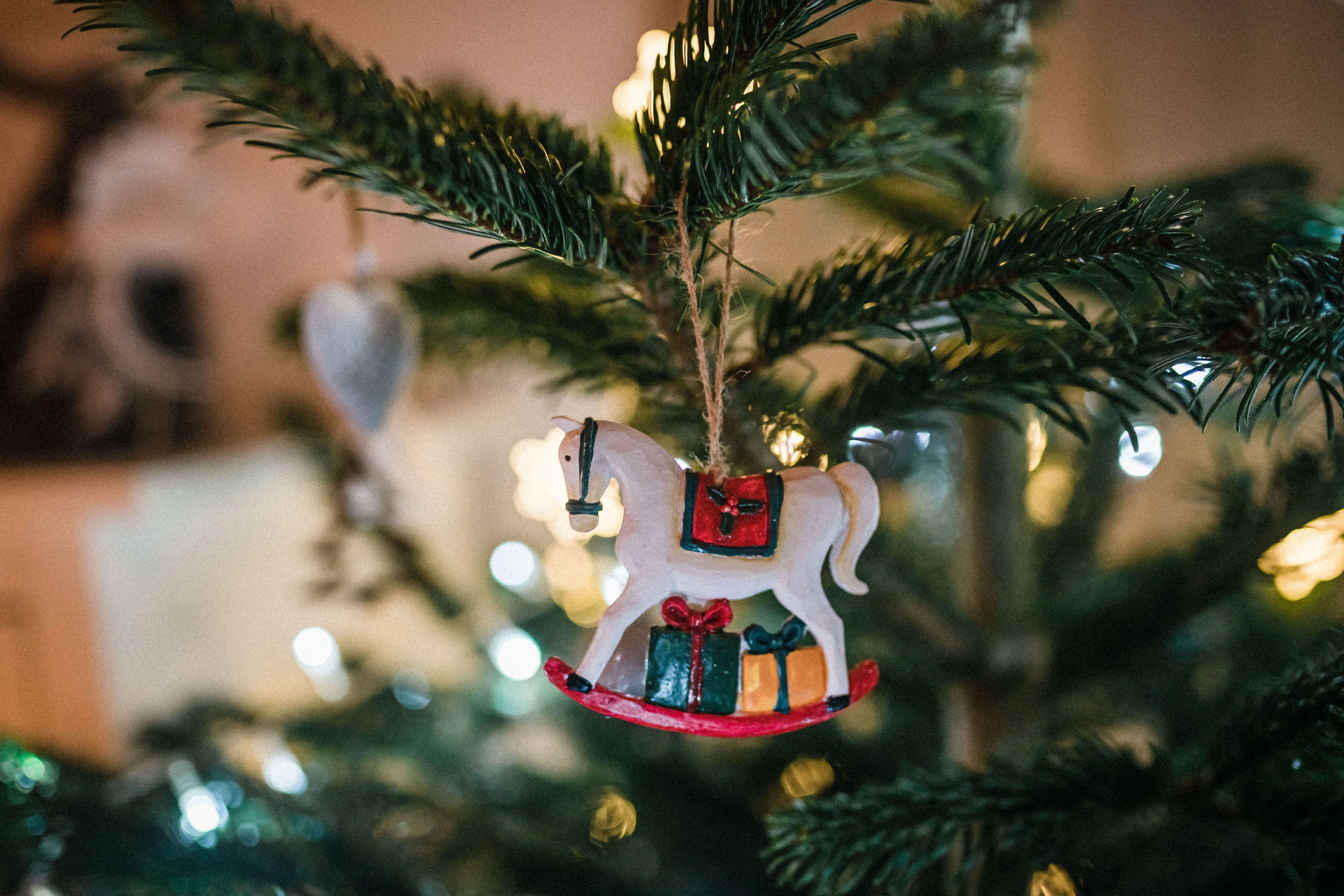 Close-up of a horse figurine ornament on a Christmas tree branch with blurred lights.