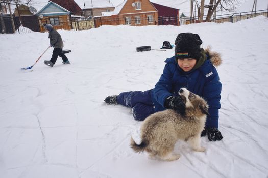 Young boys enjoying winter leisure activities with a puppy outdoors in a snowy village.