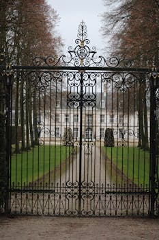 Beautiful mansion view through intricate iron gate surrounded by trees.