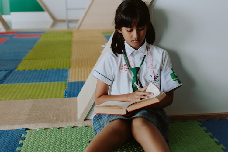 Thai Girl In School Uniform Sitting On Ground Reading Book