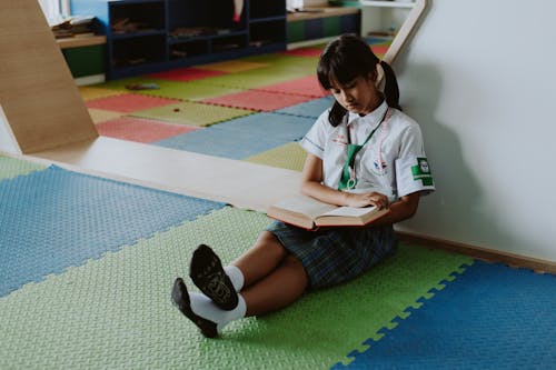 Free Thai Girl in School Uniform Sitting on Ground Reading Book Stock Photo