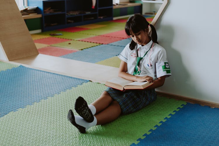 Thai Girl In School Uniform Sitting On Ground Reading Book