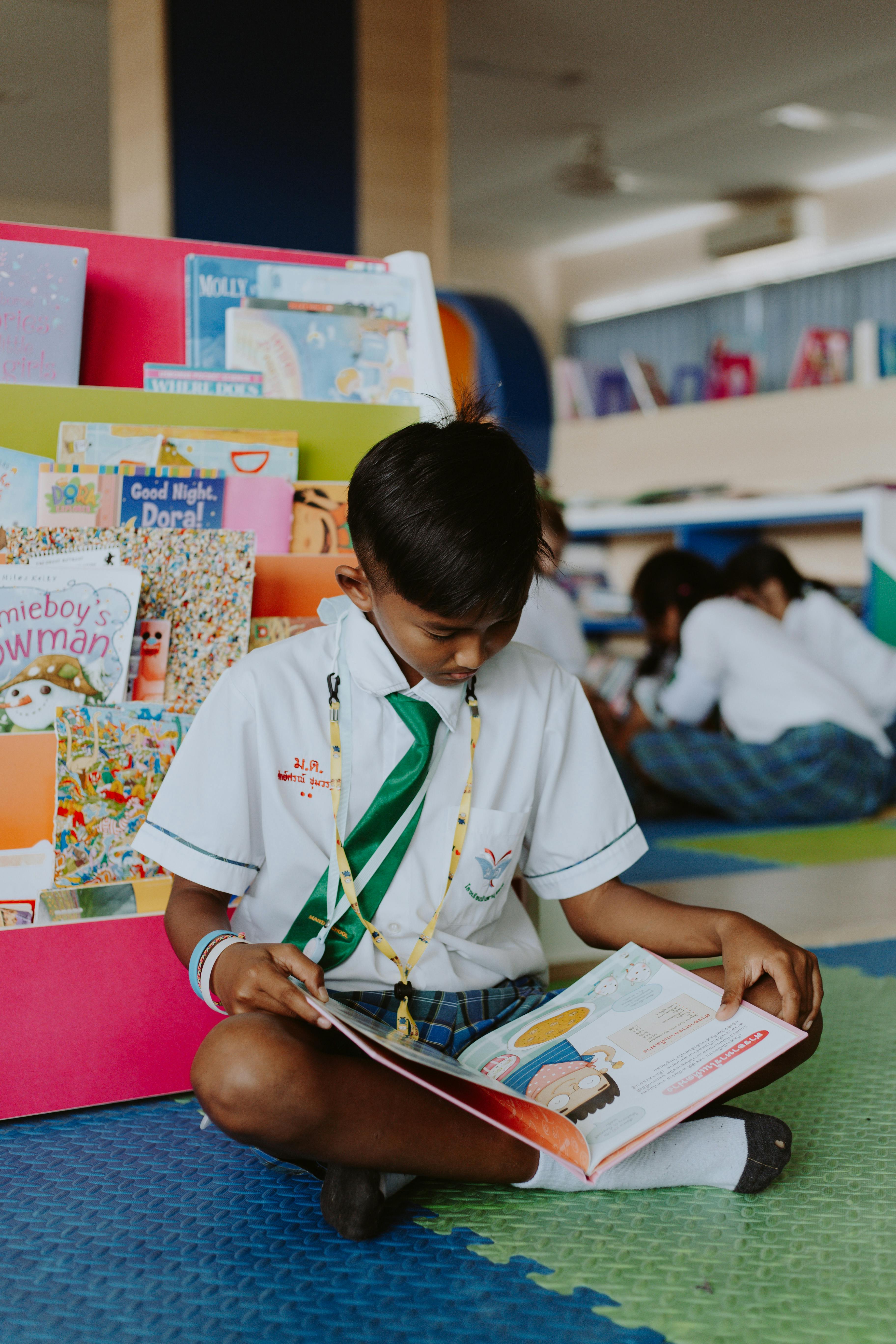 thai boy sitting cross legged on ground reading book