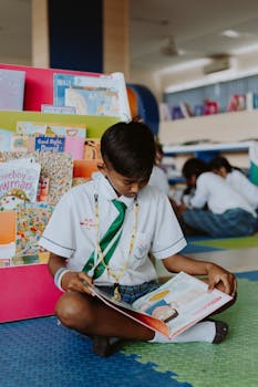 A young student reads intently on the library floor, surrounded by colorful children's books.