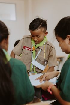 Thai students in scout uniforms studying together indoors, focused on learning.