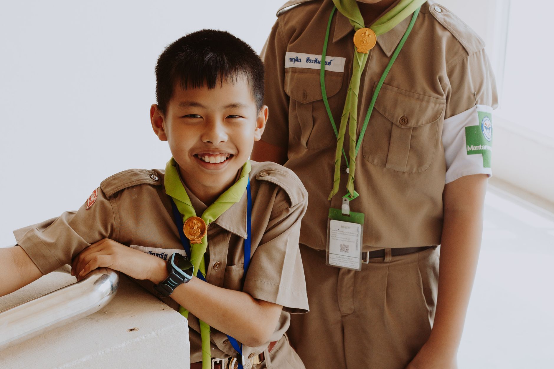 Two Asian boy scouts smiling in their uniforms indoors, showcasing camaraderie and happiness.