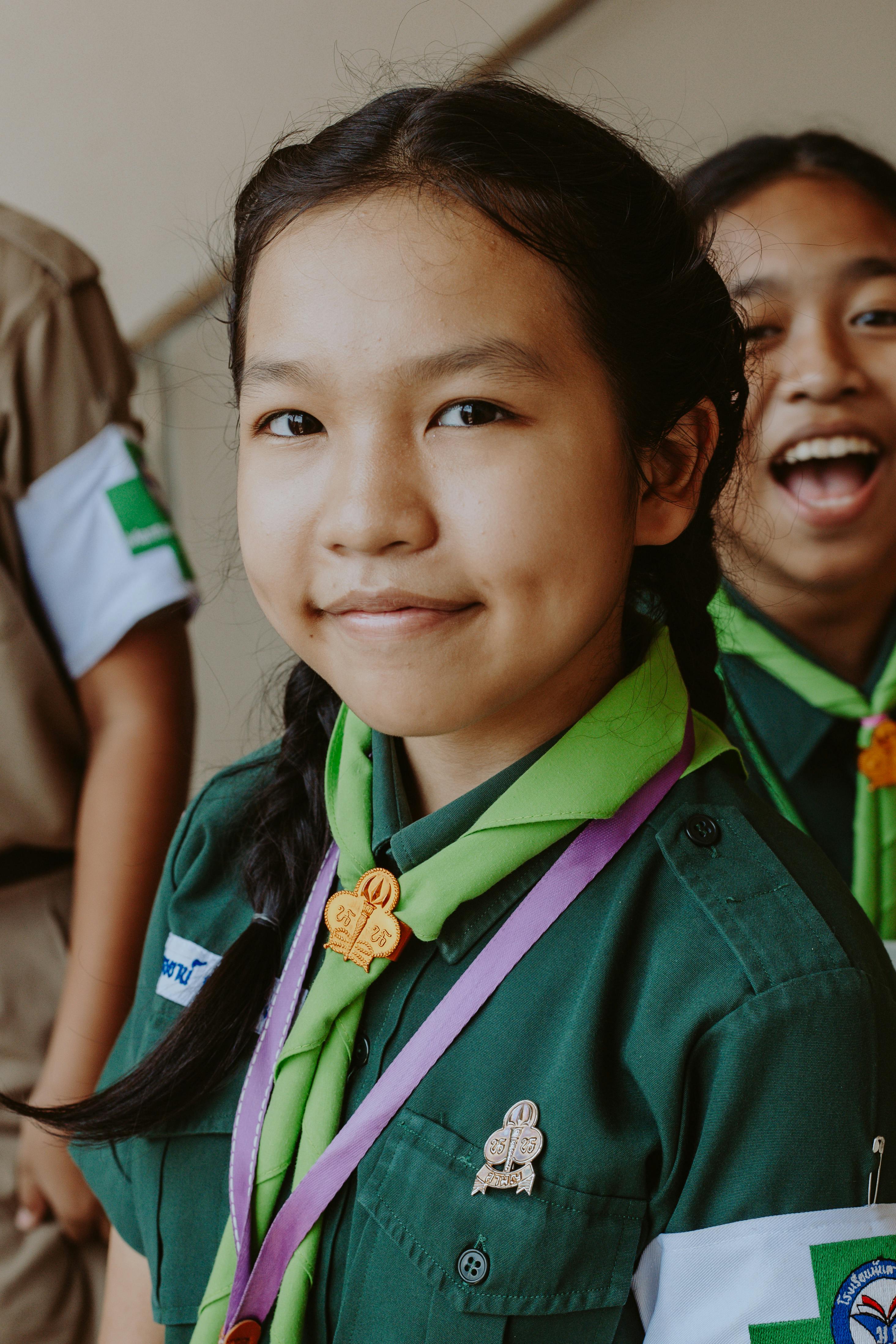 Portrait of a smiling girl scout in a green uniform and scarf, representing youth and education.