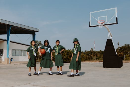Four schoolgirls in uniforms on an outdoor basketball court on a sunny day.