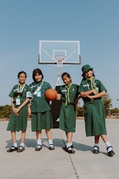 Group of school girls in uniforms posing by basketball hoop outdoors