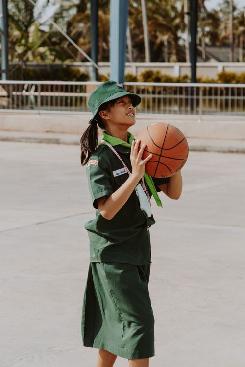 Free A smiling girl in a green scout uniform playing basketball on an outdoor court. Stock Photo
