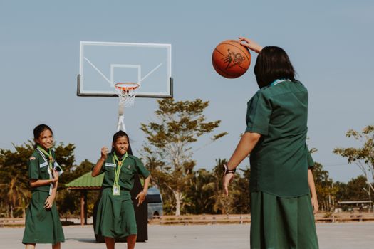 Three girls in uniform enjoying basketball on an outdoor court under sunny skies.