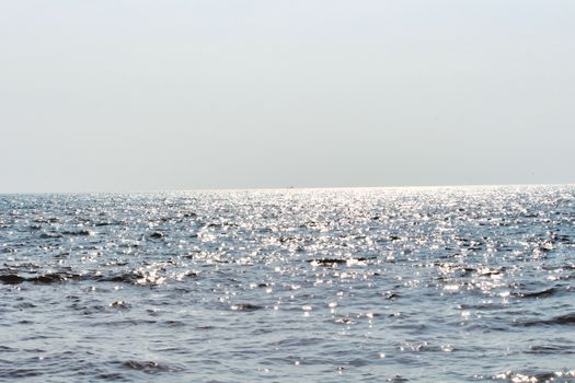 A peaceful ocean view with sparkling sunlight on the water and a clear horizon, evoking serenity.