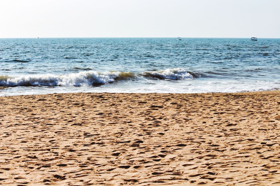 A peaceful sandy beach with gentle ocean waves under a clear sky.