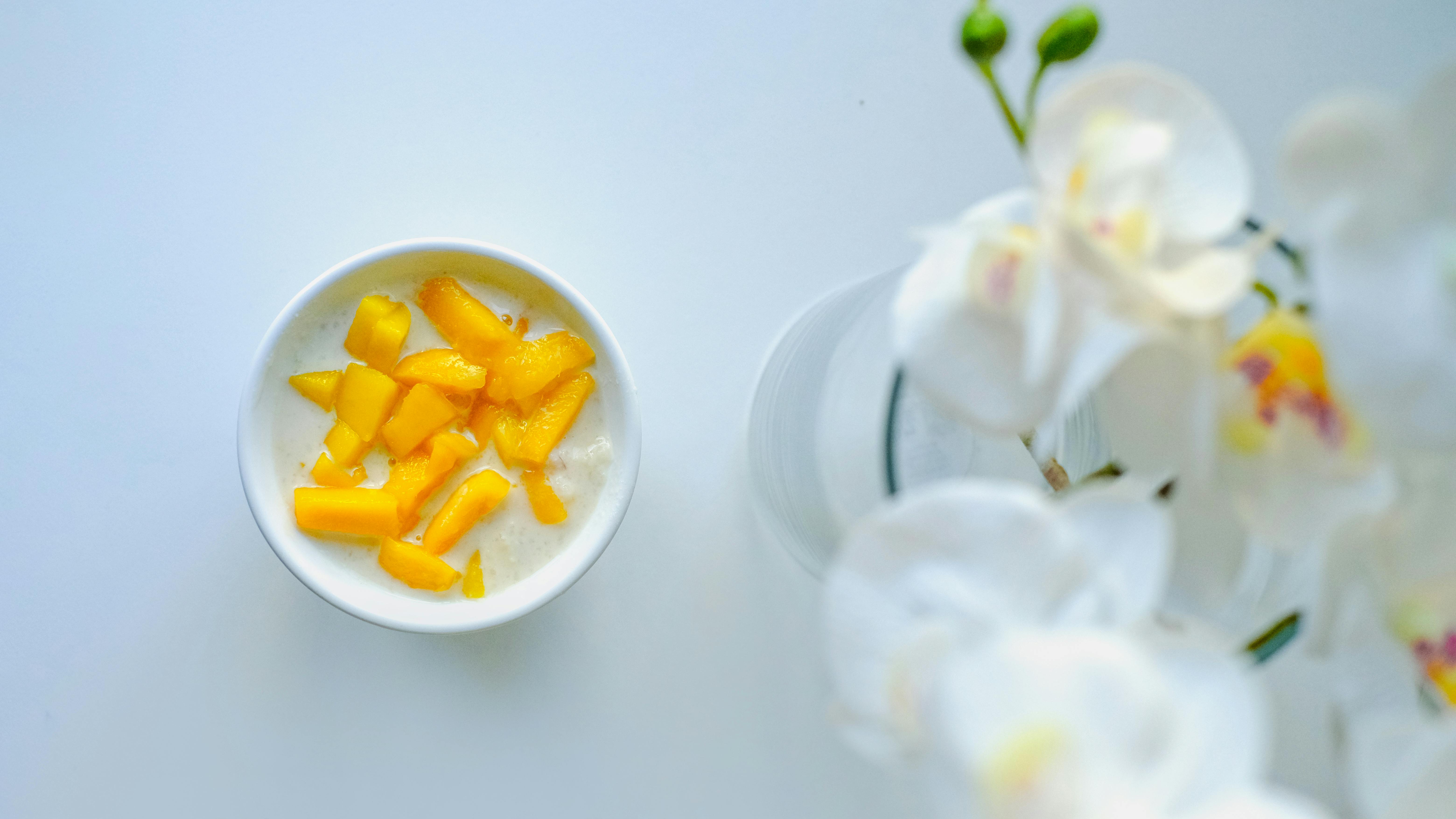 A flat lay of a bowl of mango yogurt with white orchid flowers, perfect for a healthy breakfast.