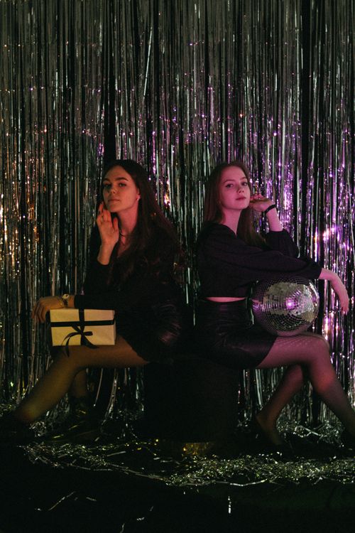 Free Two women posing with a disco ball and a gift, set against a sparkling backdrop. Stock Photo