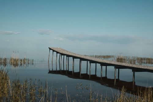 Free Tranquil scene of a wooden dock stretching over a still lake under a clear sky. Stock Photo
