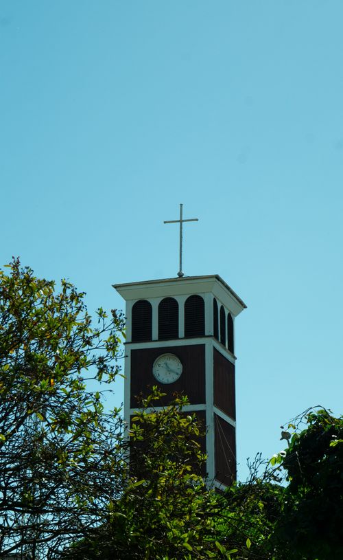Free Vertical shot of a church clock tower with a cross under a clear blue sky. Stock Photo