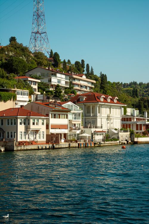 Free Charming residential waterfront view of houses along a peaceful riverbank under a clear sky. Stock Photo