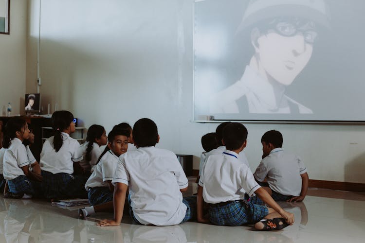 Children In School Uniforms Watching Movie In Classroom