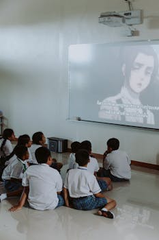 Group of school children watching anime on a projector screen indoors.