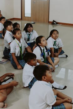 Group of school children in a classroom sitting on the floor, listening intently to a lesson.