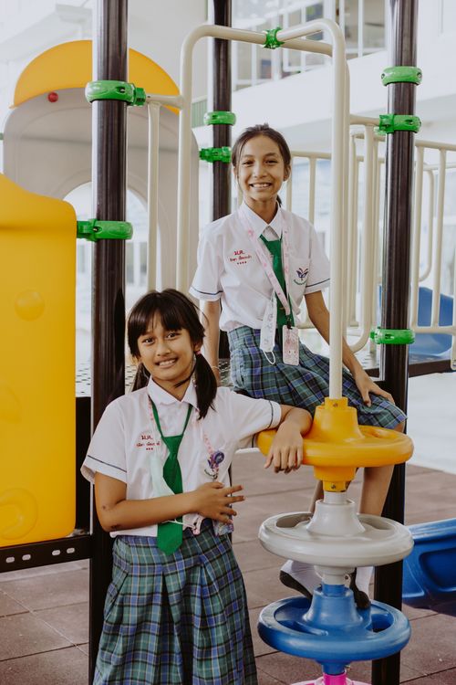 Free Two girls in school uniforms smiling at a playground, conveying friendship and education. Stock Photo