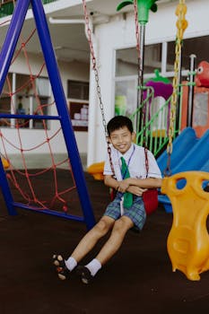 Joyful child in school uniform enjoying playtime on a swing at a colorful playground.