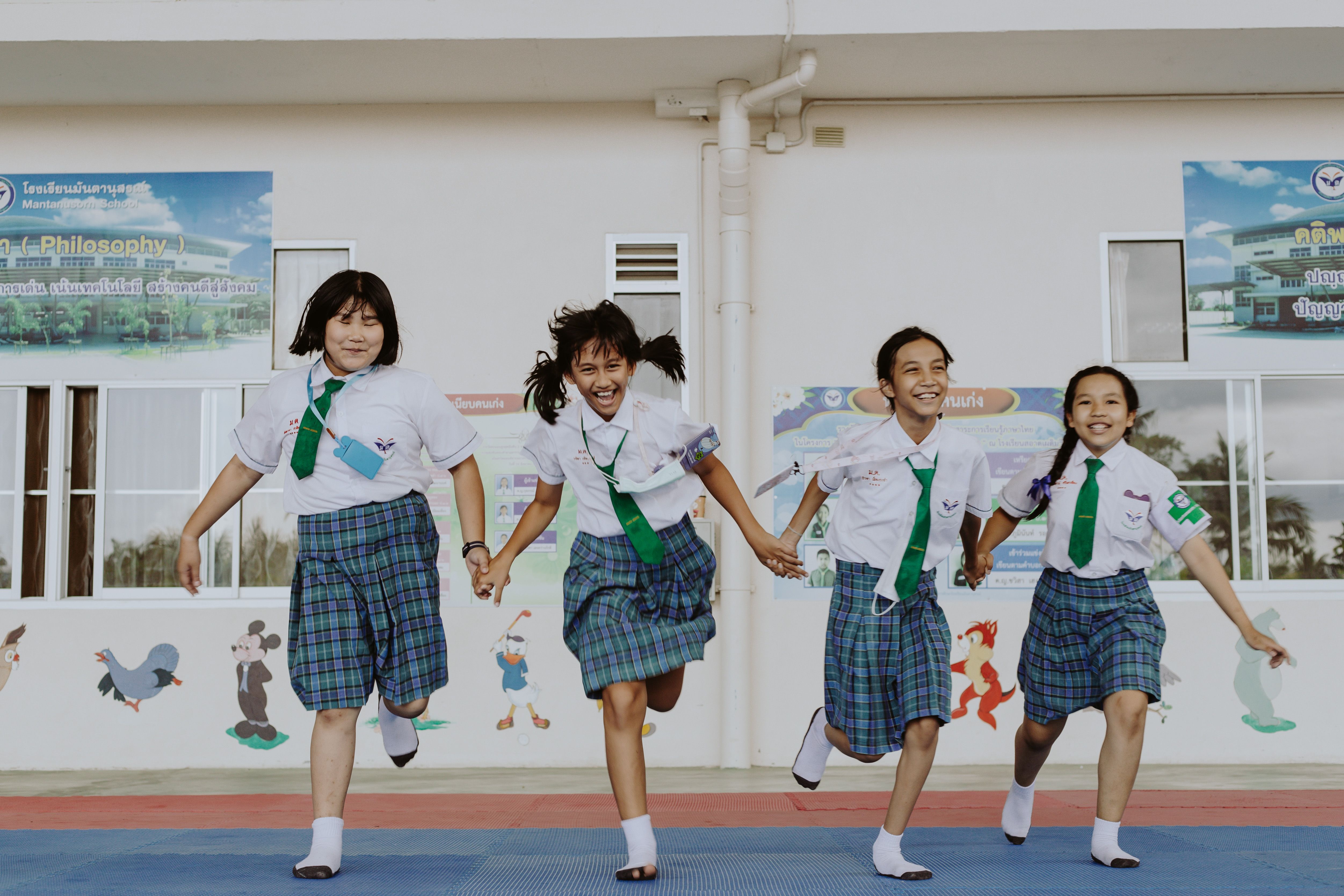 Asian schoolgirls in uniforms joyfully running hand-in-hand outdoors.