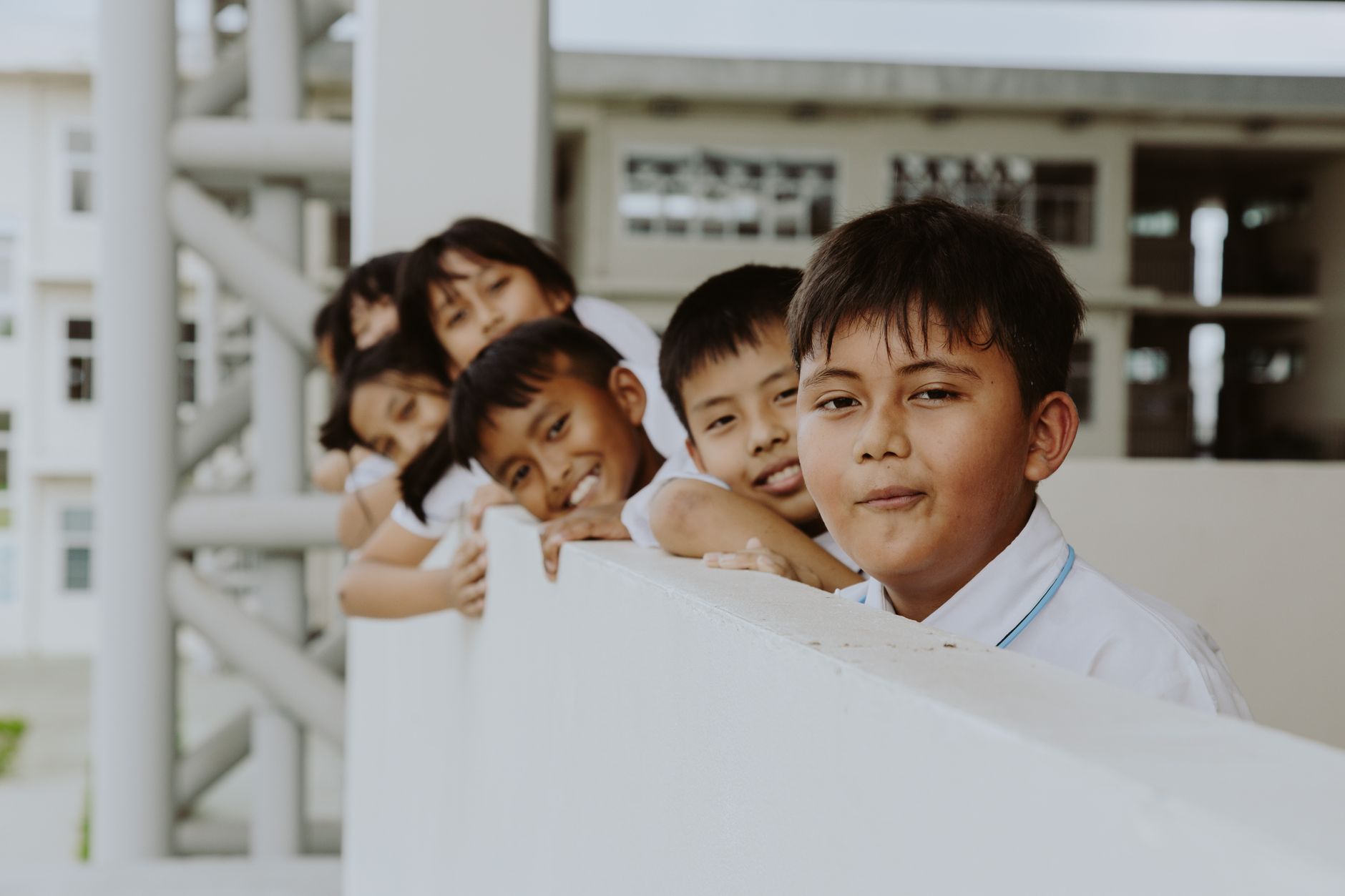 Groep kinderen leunend op de reling van de schoolgang, glimlachend en speels.