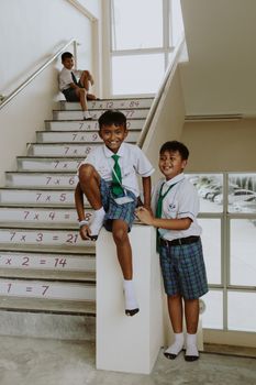 Three boys in school uniforms smiling on a staircase with math formulas.