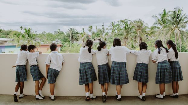 Children in school uniforms leaning against a balcony wall outdoors, looking at nature.