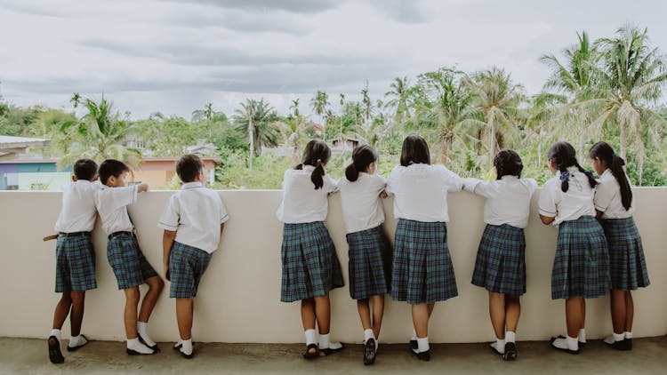 Rear View Of Boys And Girls In School Uniforms Standing On Terrace