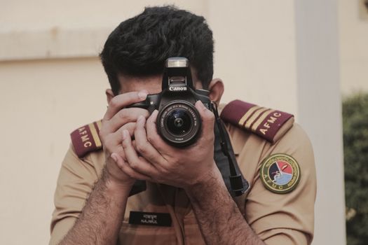 A military photographer in uniform aiming a camera at the viewer, outdoors.