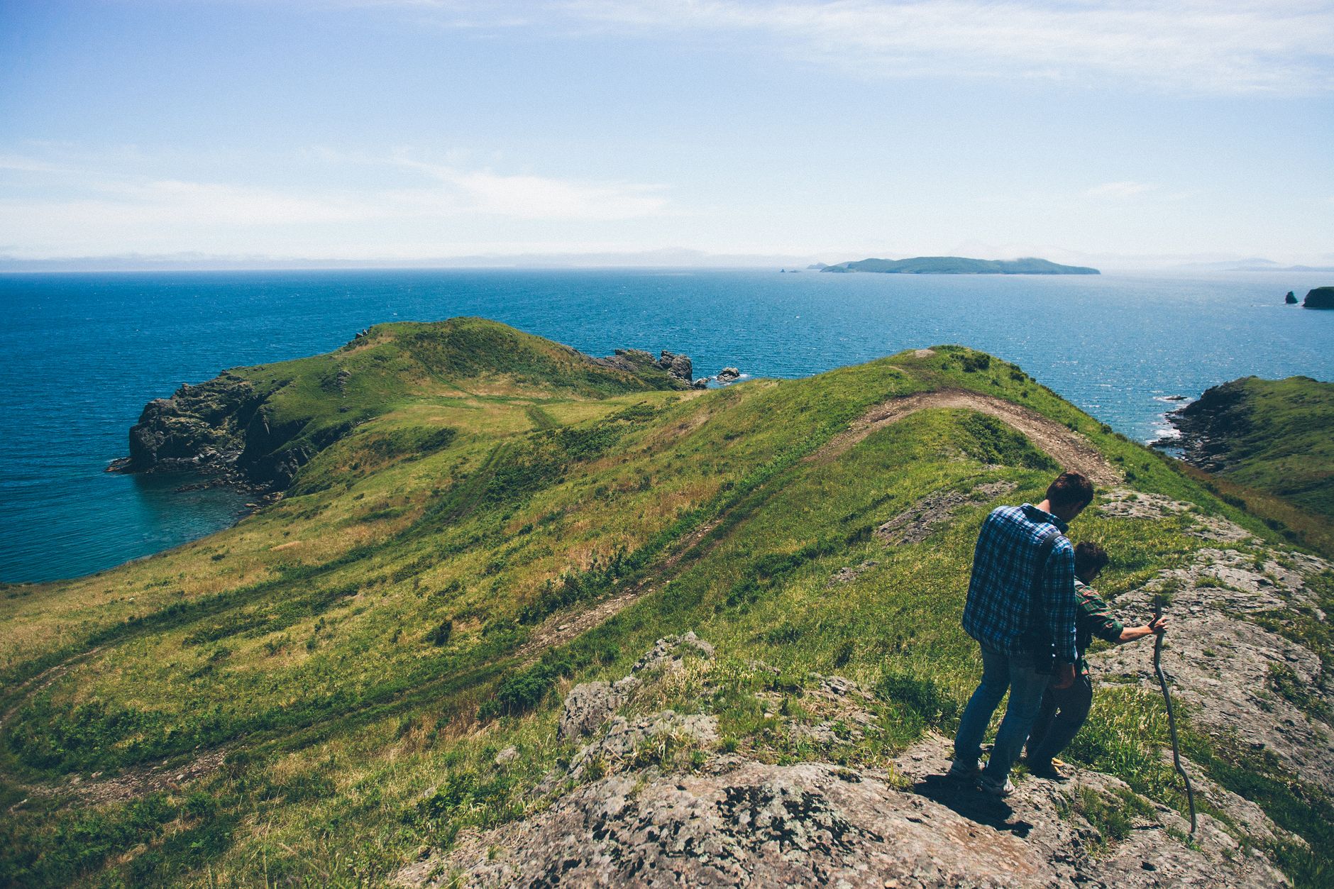 Two people hike along a scenic coastline with blue sea views under a clear sky.