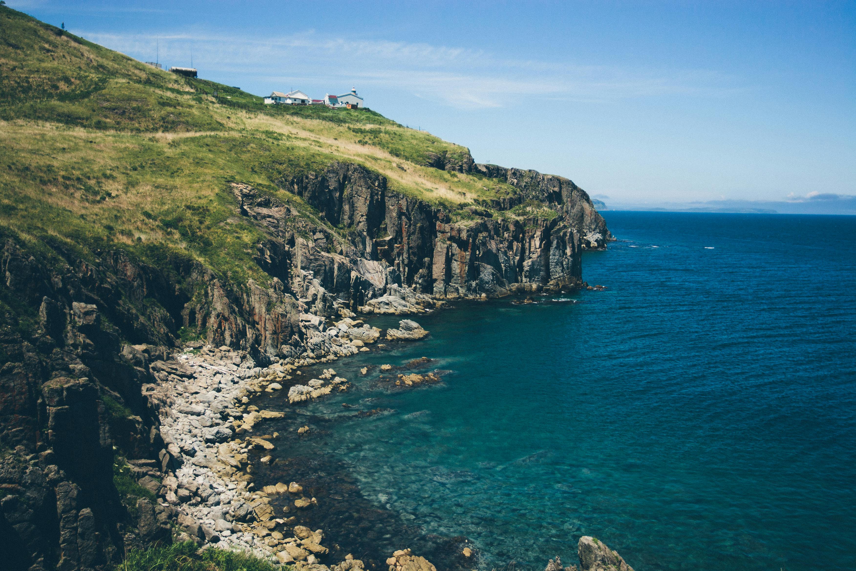 令人惊叹的岩石海岸线景色，青草悬崖上的房屋和充满活力的蓝色大海