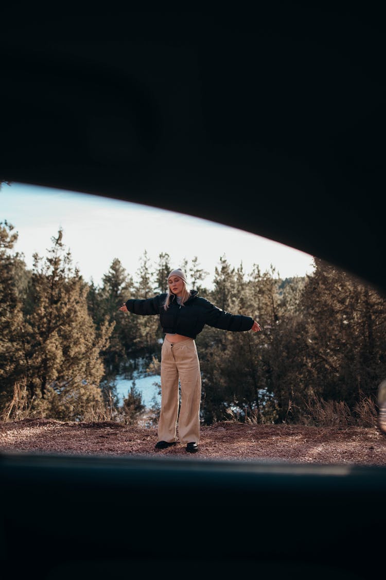 Blonde Woman In Black Jacket And Khaki Pants Standing Near The Trees 