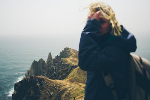 Free Blonde Person in Blue Hoodie Jacket Looking Back While Standing on Green Mountains Stock Photo