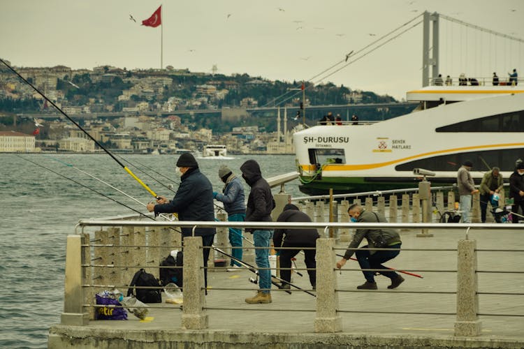 Men Fishing On A Pier And Ferry In Background