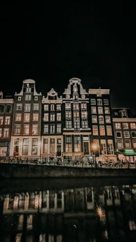 Beautiful Amsterdam canal houses illuminated against the night sky reflecting on water.